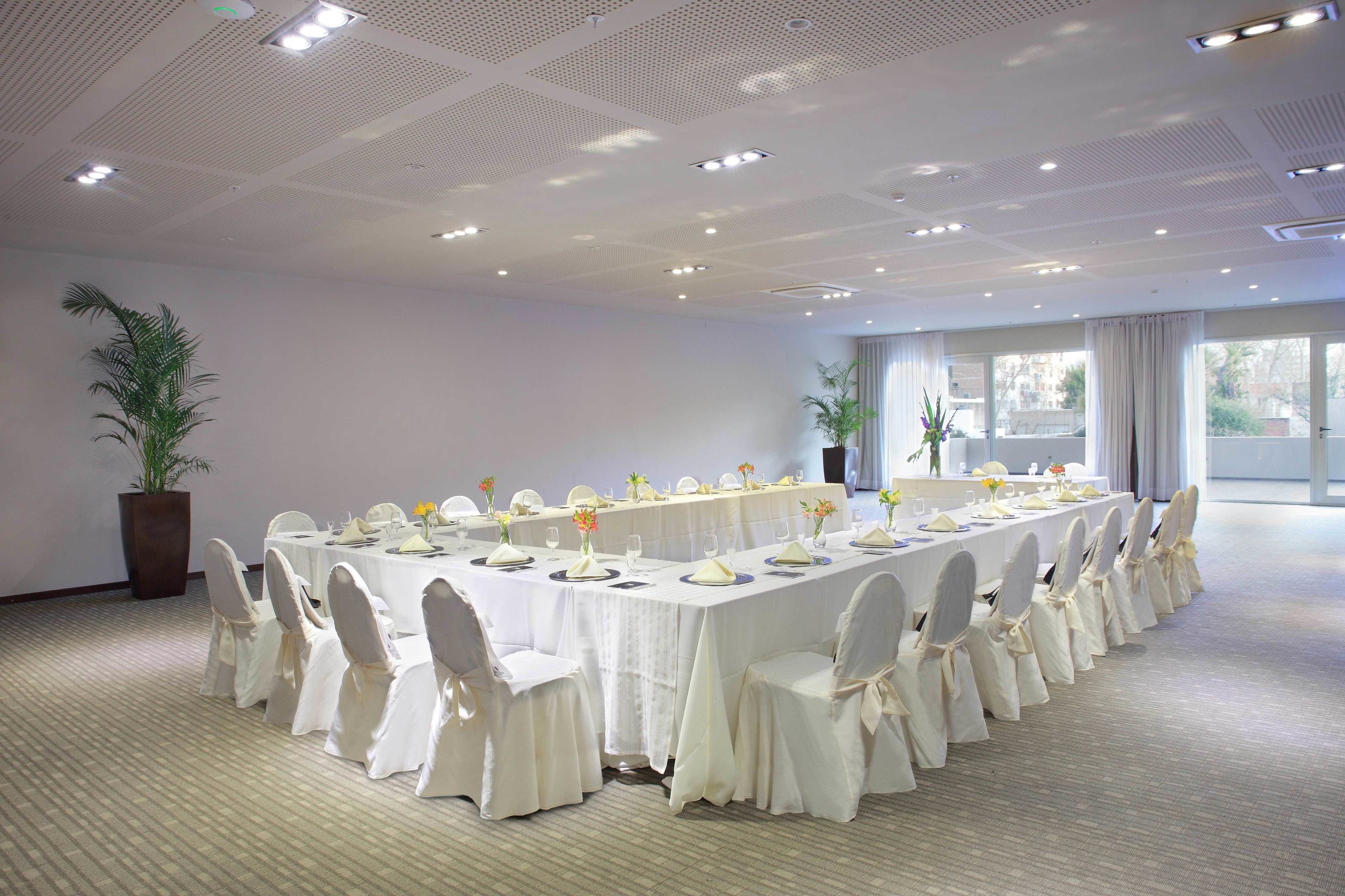 A conference room with a long table set for a formal event, surrounded by chairs with white covers.