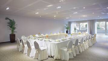 A conference room with a long table set for a formal event, surrounded by chairs with white covers.