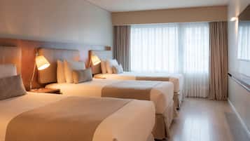 Habitación de hotel con dos camas, cada una con mesita de noche y lámpara, un ventanal grande con cortinas y suelo de madera.