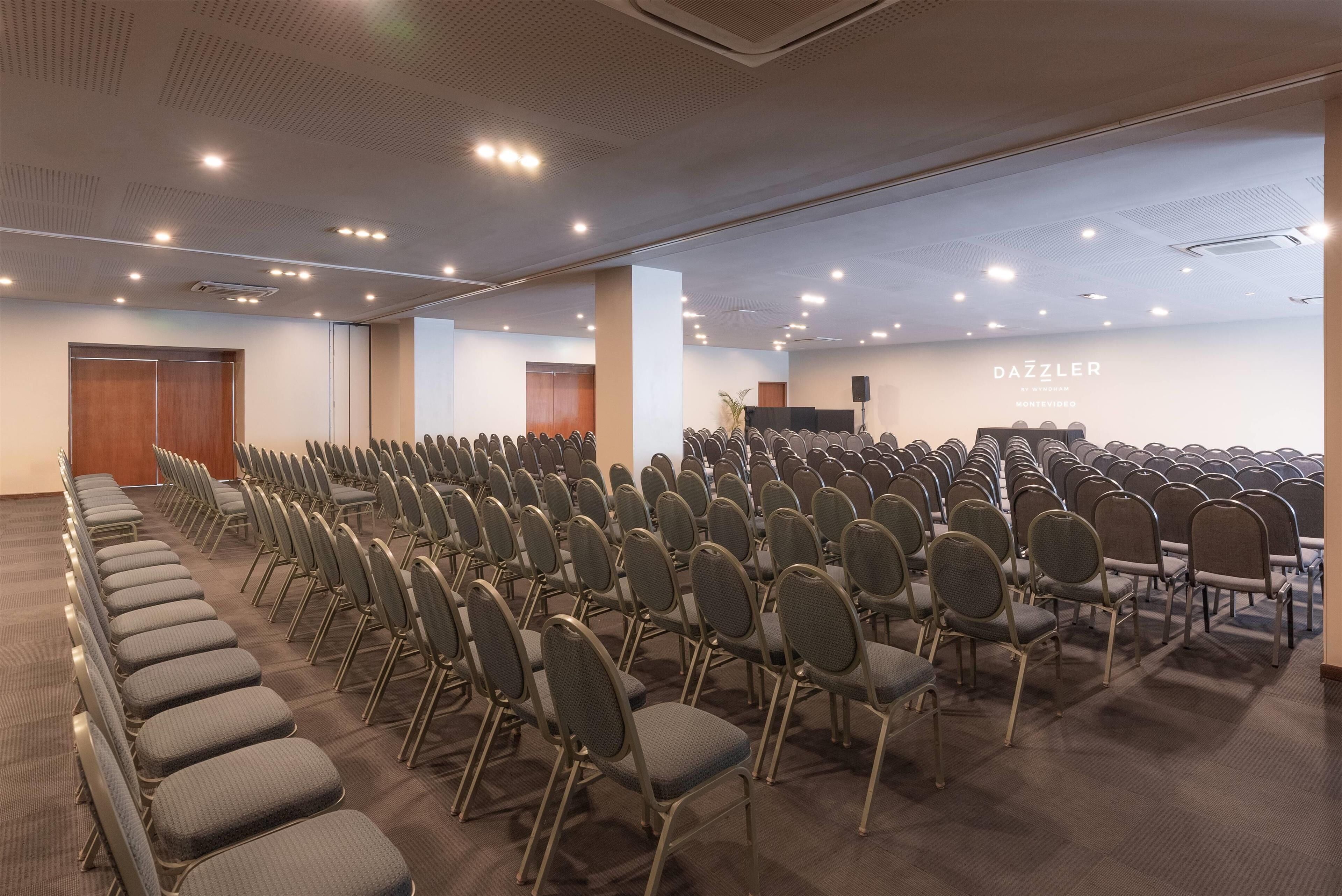 Un salón de conferencias con filas de sillas, un atril y una pared con el texto "DAZZLER".