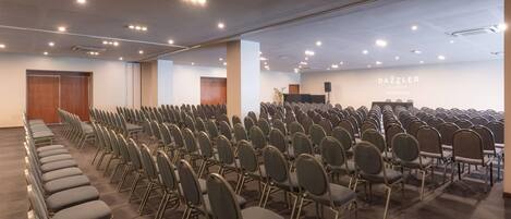 Un salón de conferencias con filas de sillas, un atril y una pared con el texto "DAZZLER".