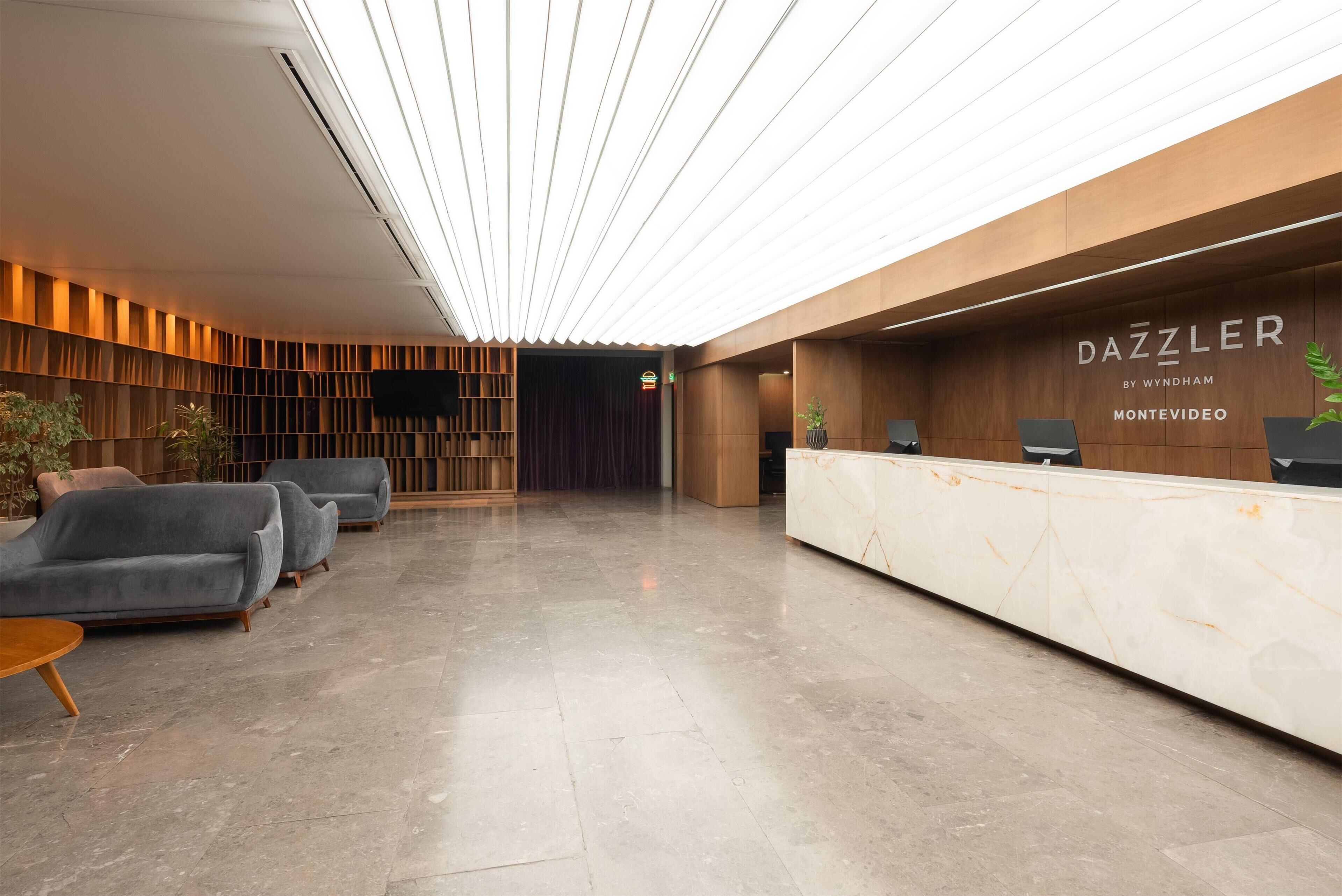A modern reception area with a marble reception desk, grey sofas, and a wooden wall with a vertical slat design.