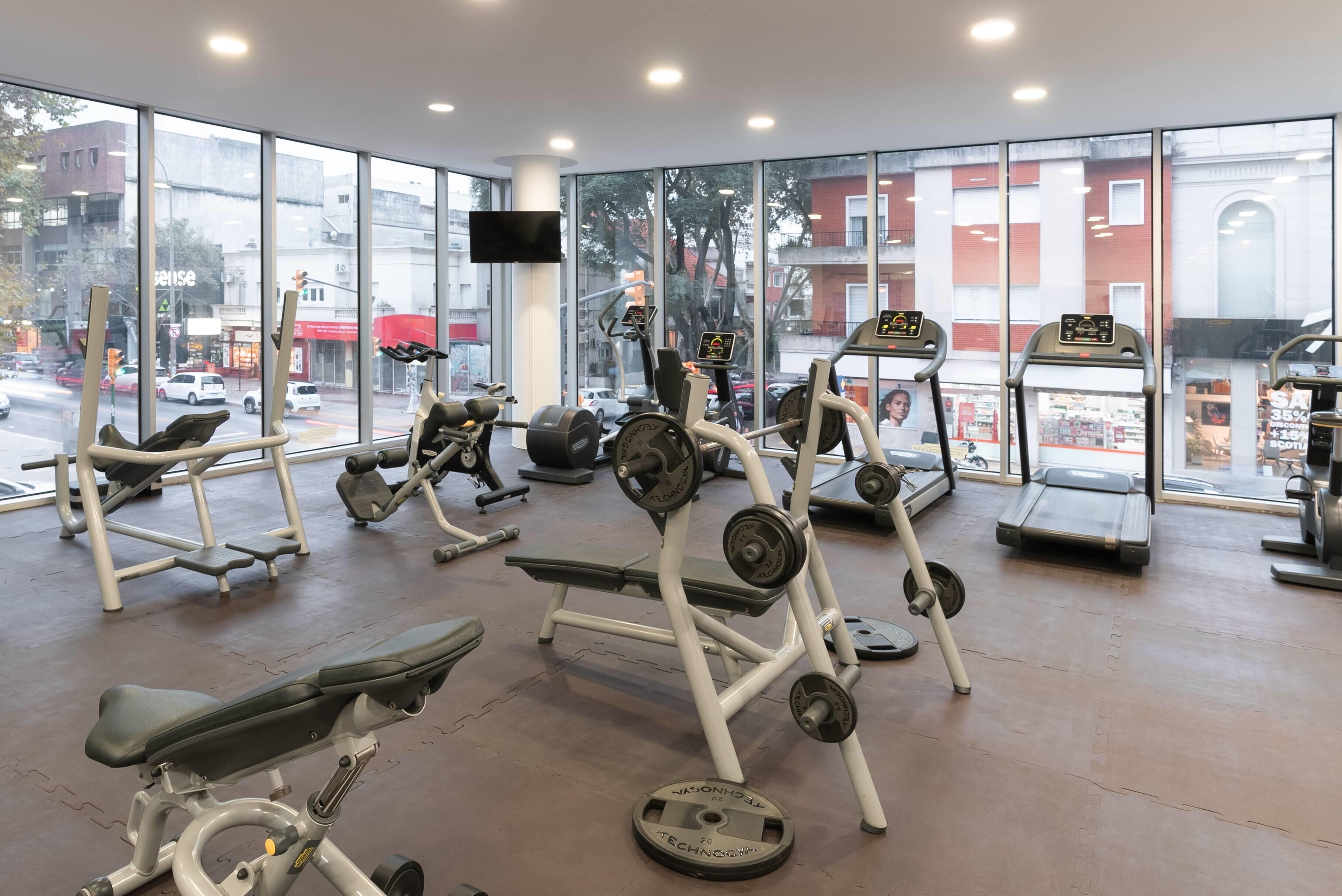 A gym with various exercise equipment, large windows, and a view of the street outside.