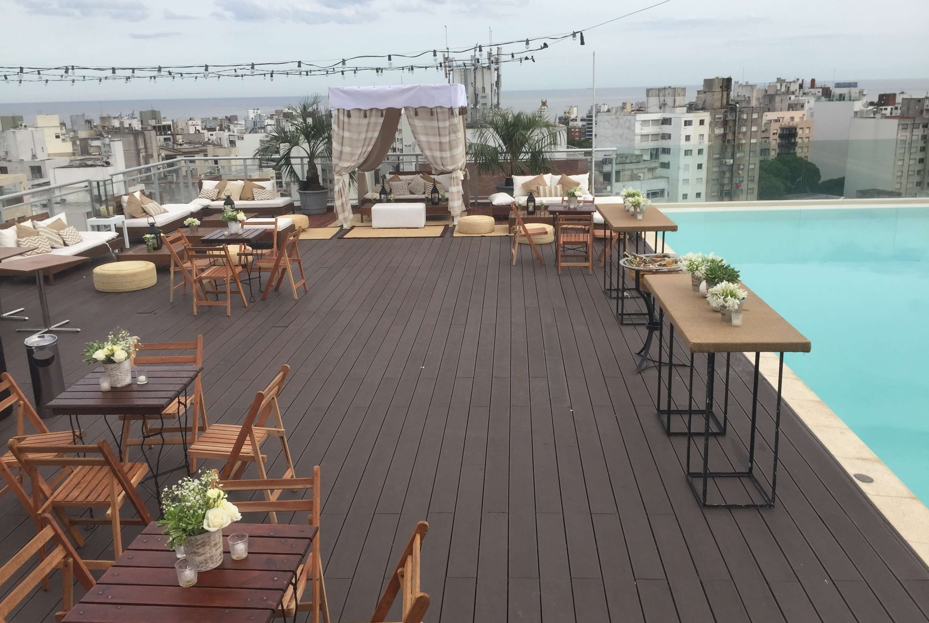 A rooftop terrace with wooden furniture, a pool, and city views.