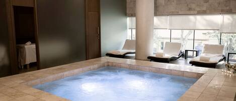 Un área de spa con un amplio jacuzzi, asientos y vistas al exterior.