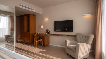 Una habitación de hotel moderna con un escritorio de madera, un sillón cómodo, un televisor de pantalla plana en la pared y un amplio armario.