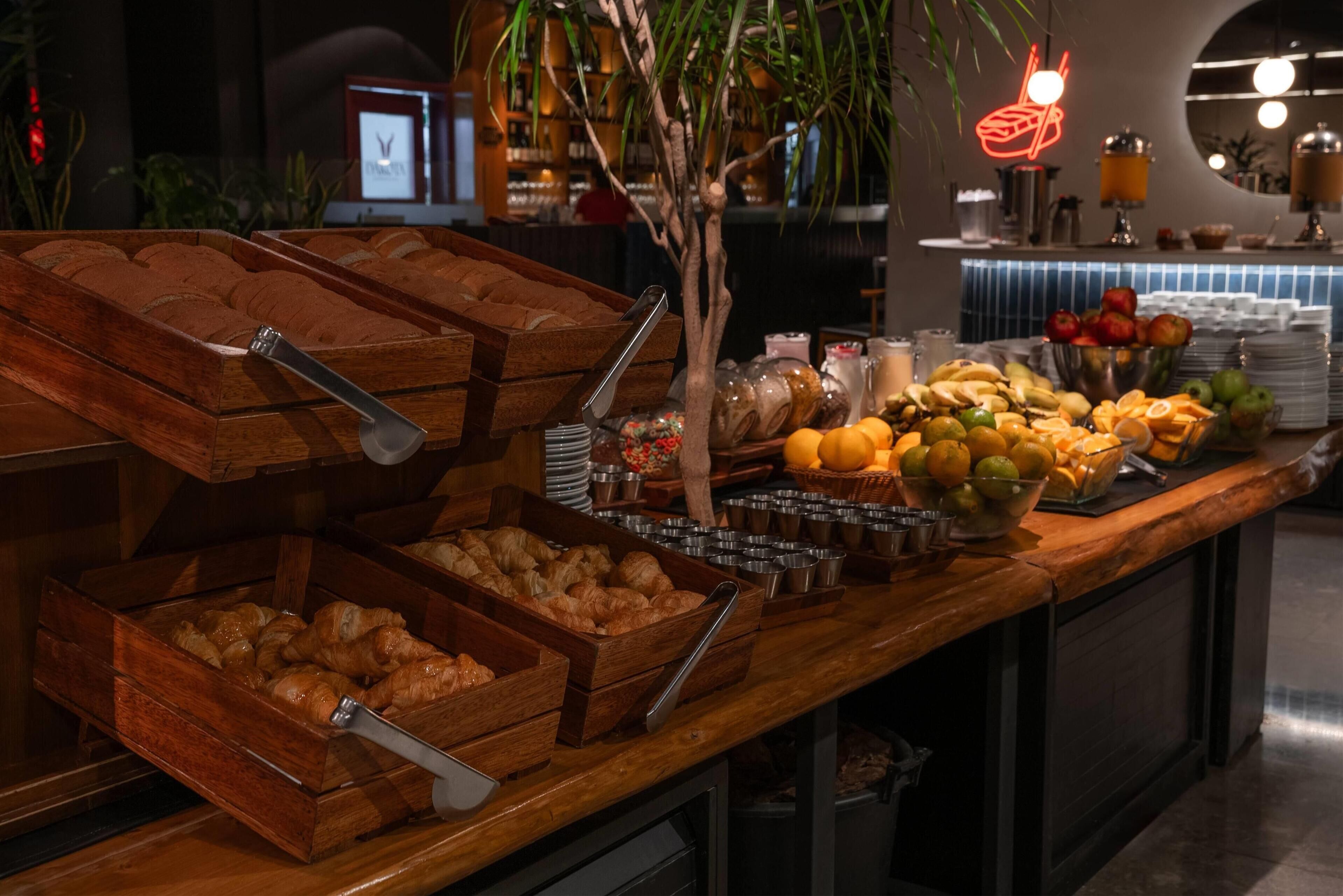 A buffet with wooden serving trays, a variety of fruits, and a neon sign in the background.