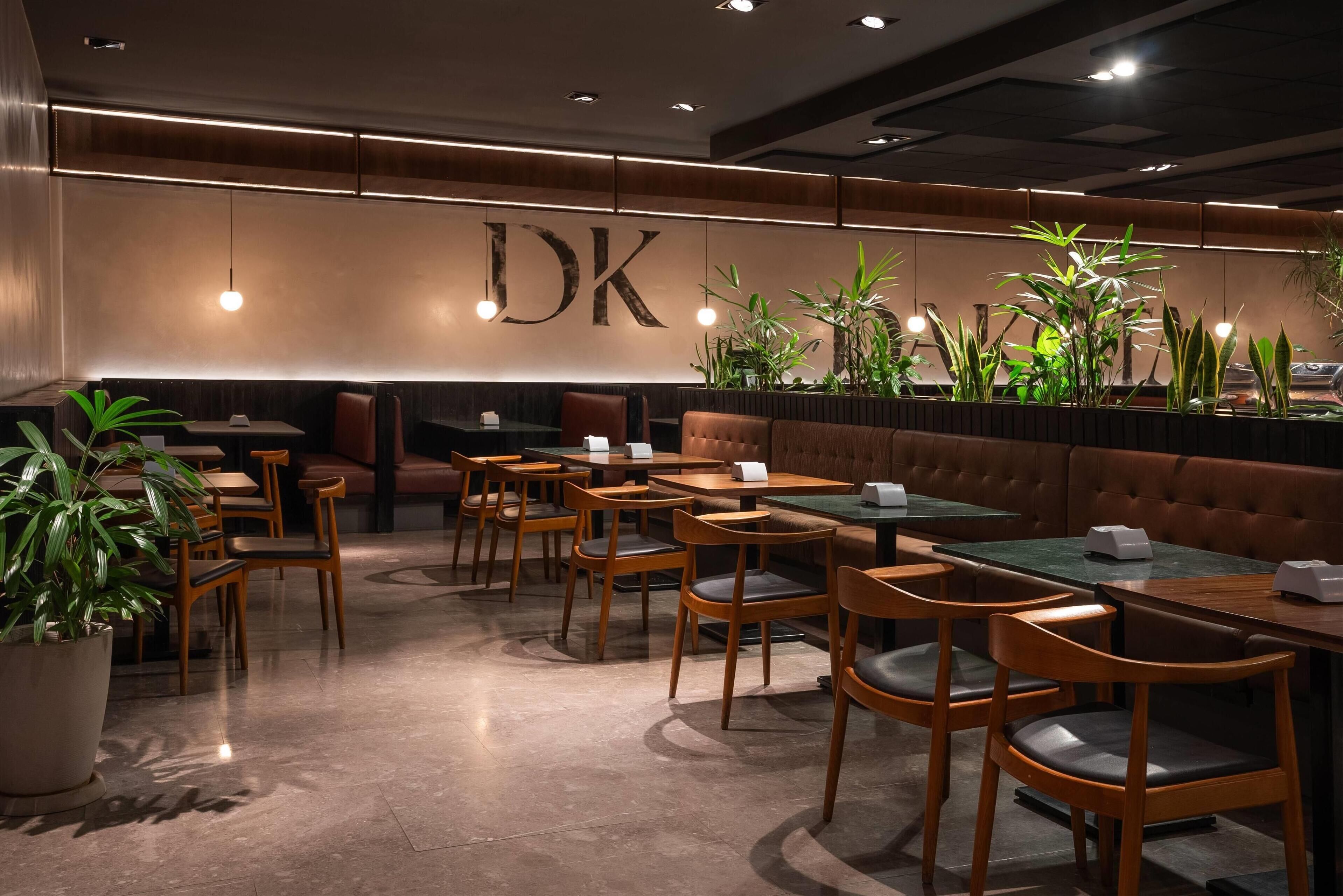 Interior de restaurante con mesas y sillas de madera, un gran letrero 'DK' en la pared y plantas en macetas.