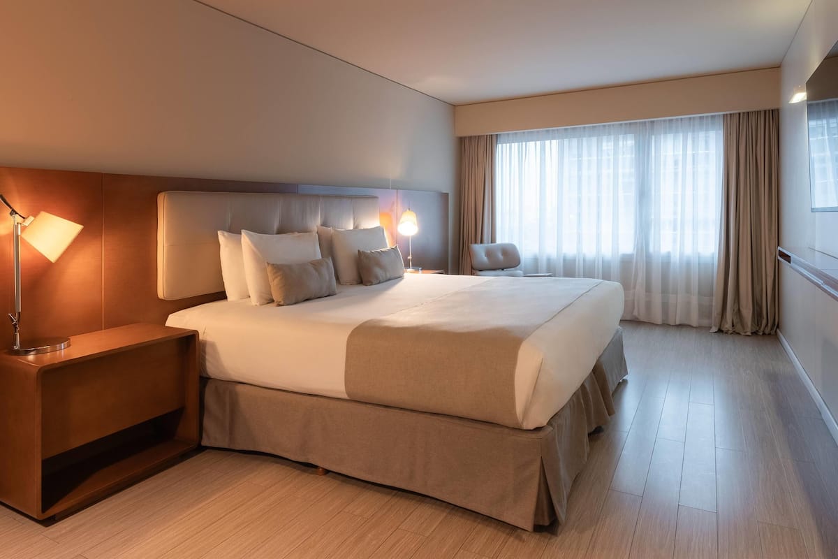A hotel room with a large bed, a nightstand, a lamp, and a window with curtains.
