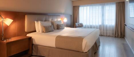 Habitación de hotel con una cama grande, una mesita de noche, una lámpara y una ventana con cortinas.