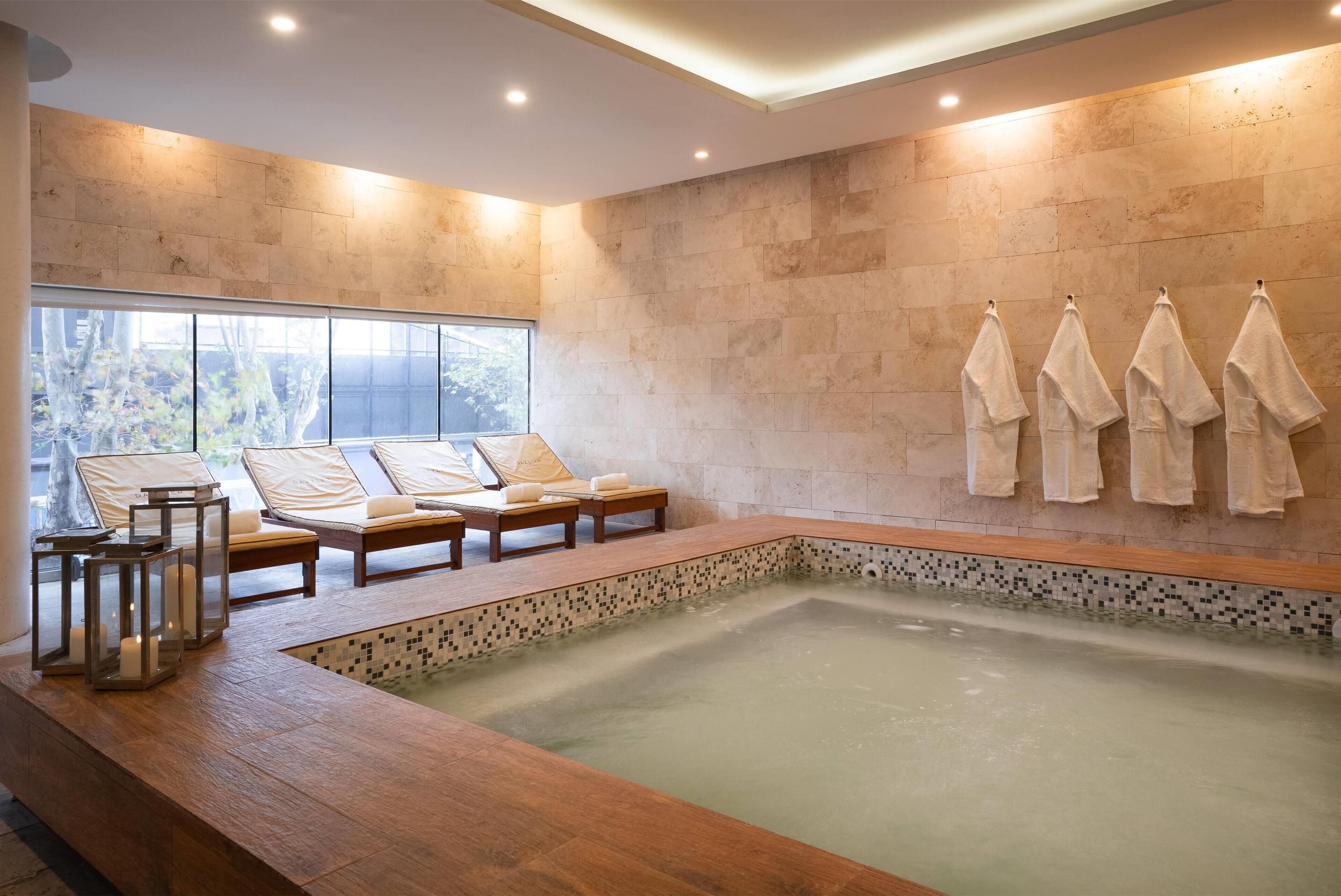 Un área de spa con una bañera grande, tumbonas de madera y una pared de azulejos.