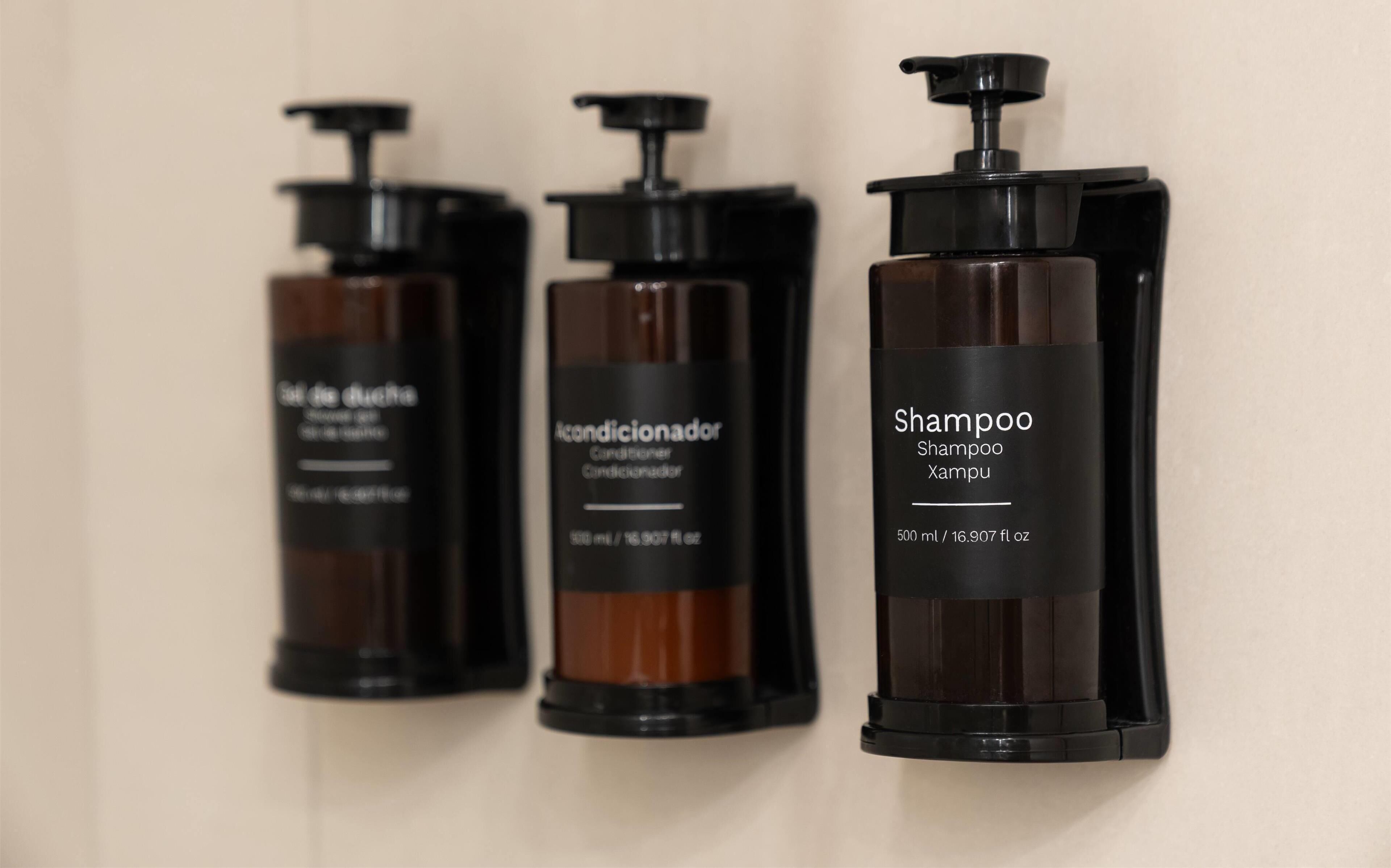 Three bottles of shampoo with black pumps and labels, arranged against a plain wall.