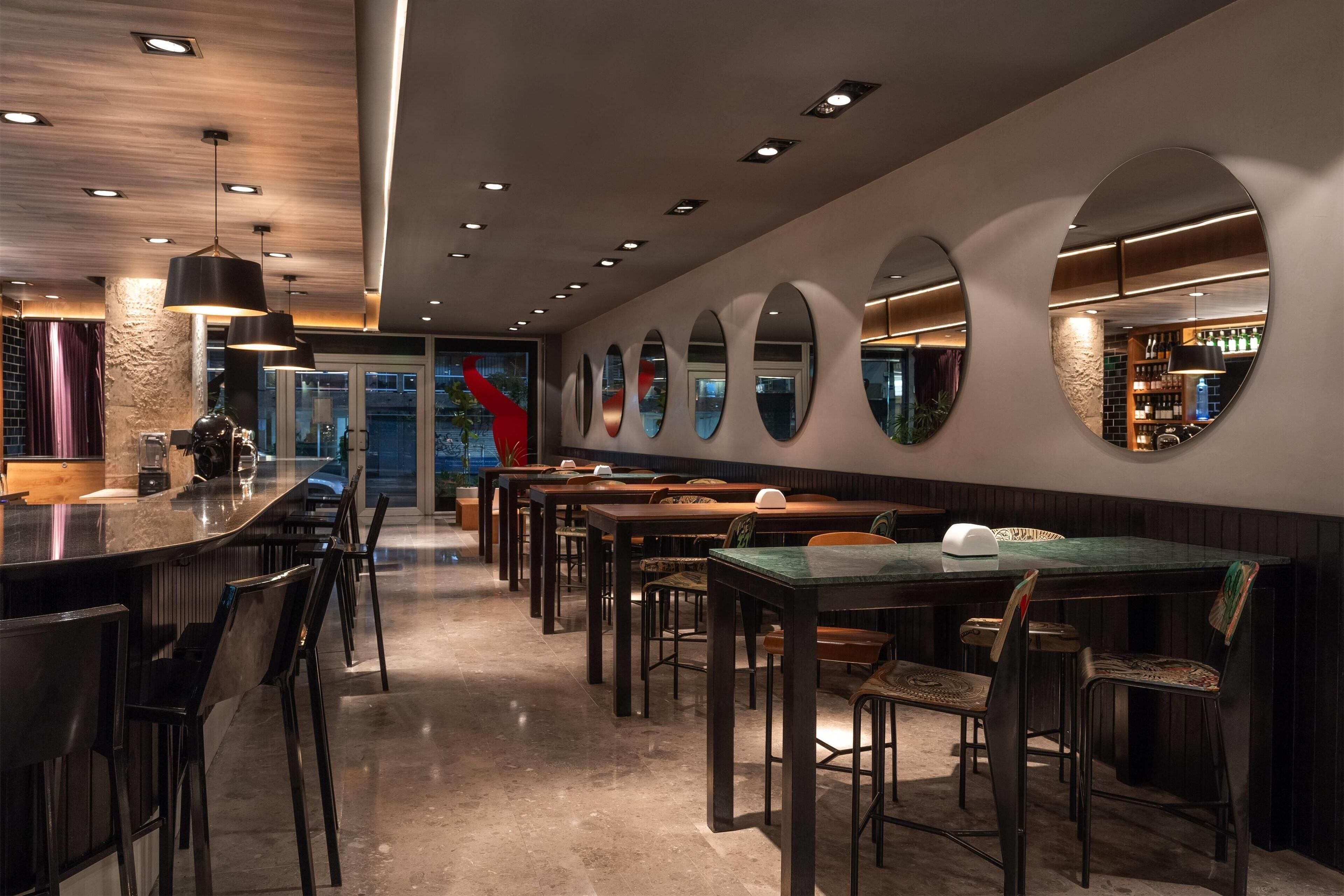 Un espace bar moderne doté d’un long comptoir, de plusieurs tables et de chaises pour s’asseoir.