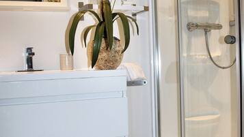 A modern bathroom with a glass shower enclosure, a white vanity with a plant, and a small wicker basket.