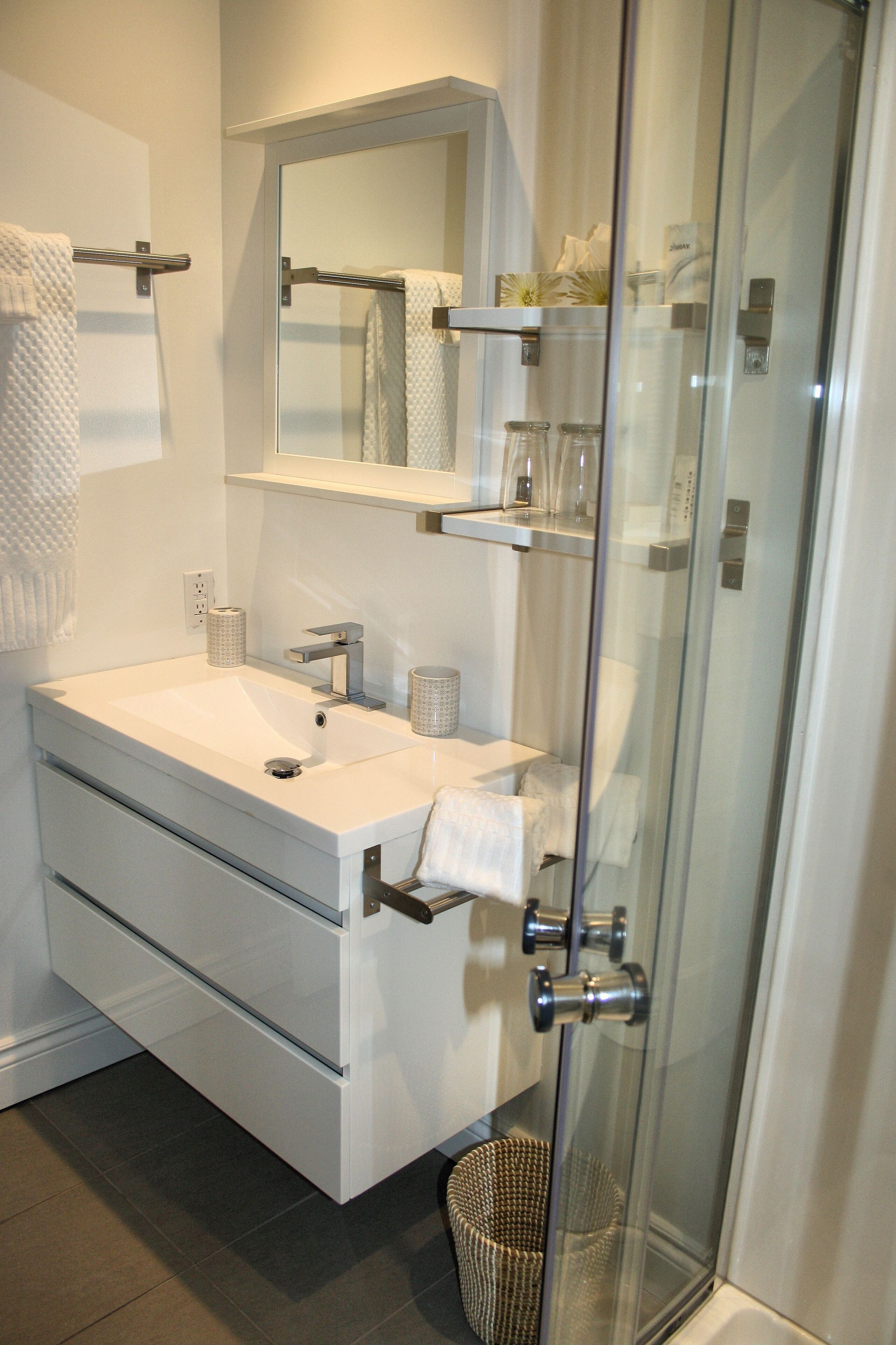 A modern bathroom with a white sink, mirror, and glass shower enclosure.