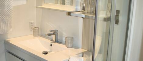 Ein modernes Badezimmer mit einem weißen Waschbecken, Spiegel und einer Duschkabine aus Glas.