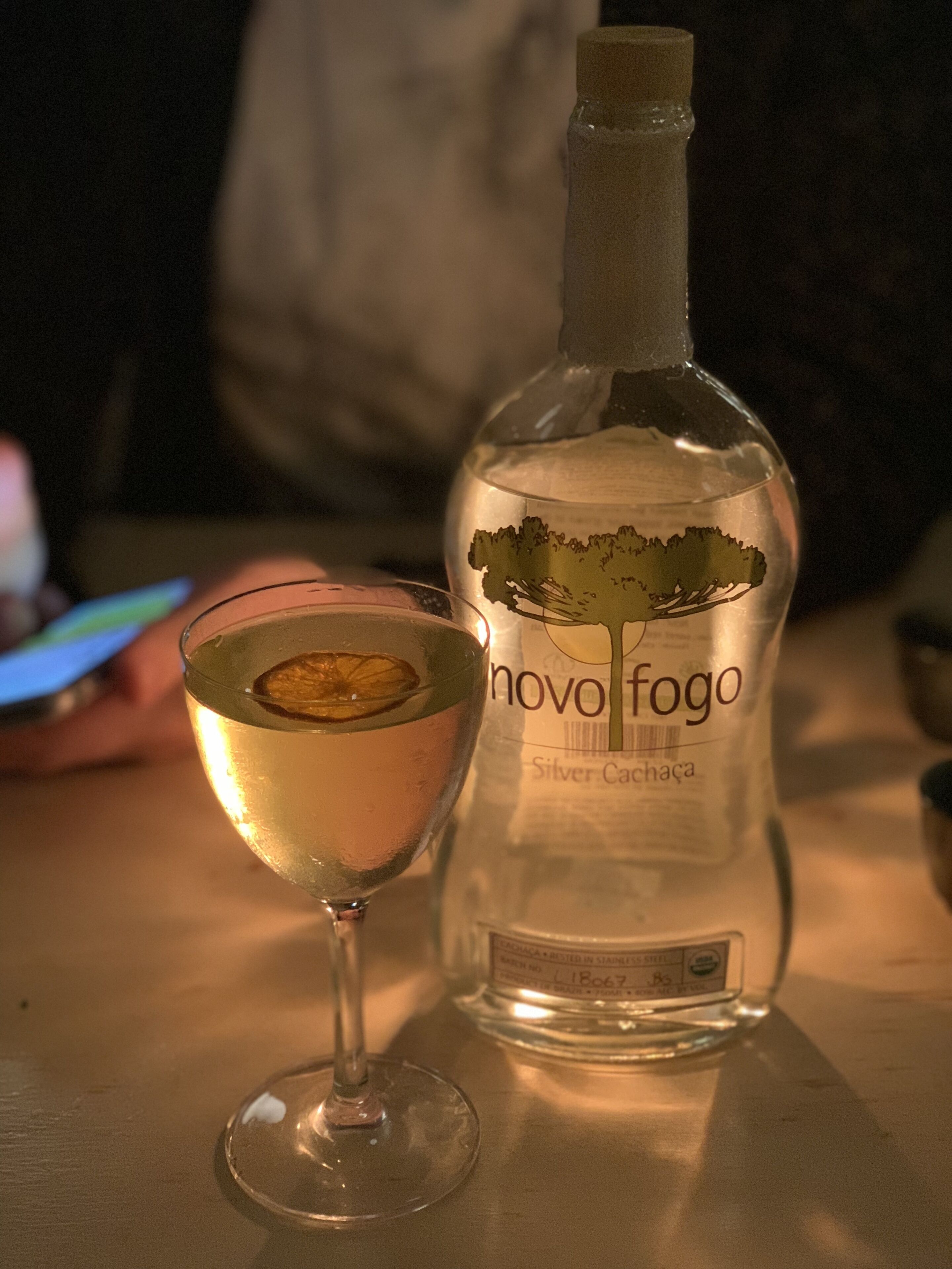 A bottle of Novo Fogo Silver Cachaca next to a glass with a slice of citrus.