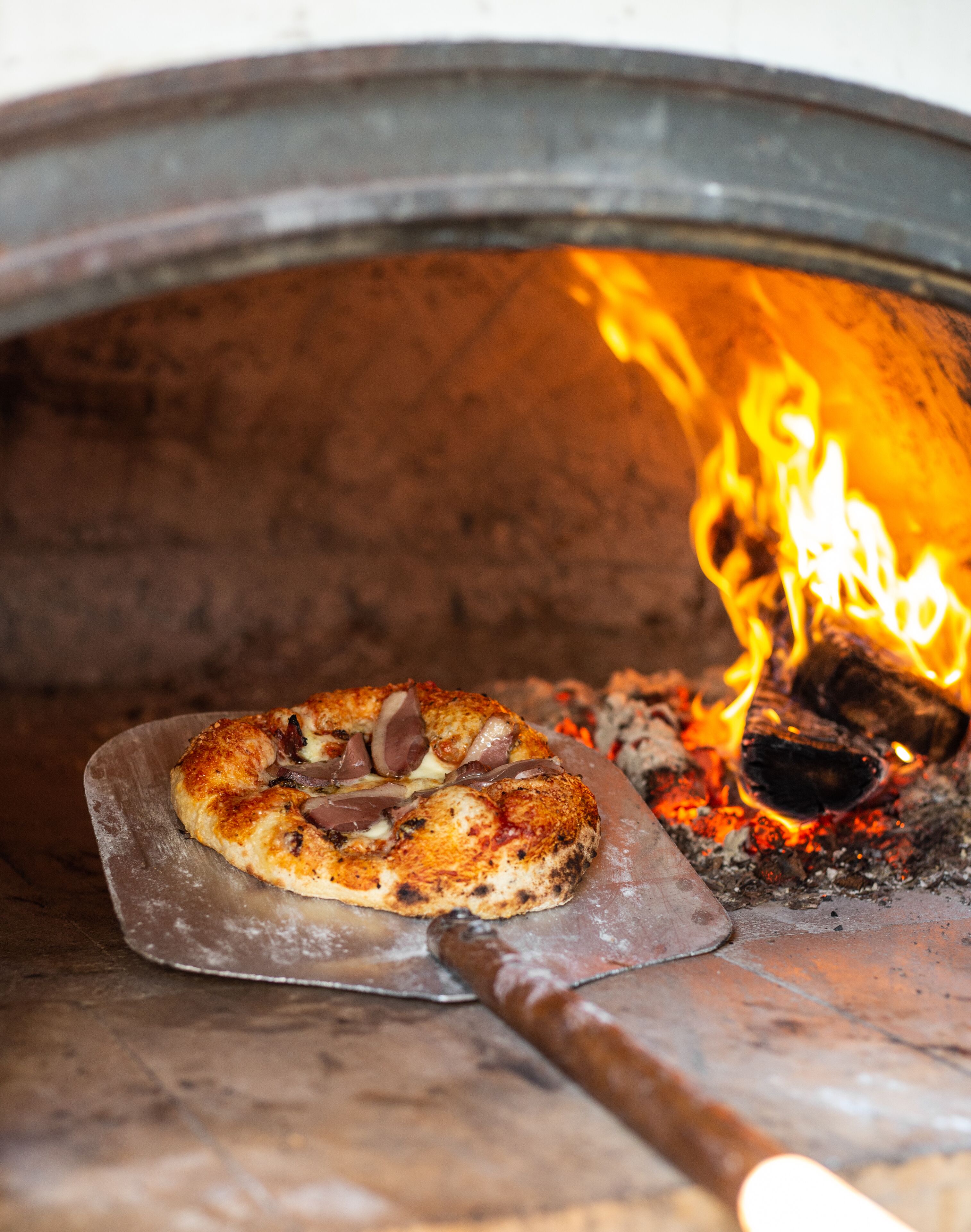 Una pizza en un horno de leña con llamas visibles.