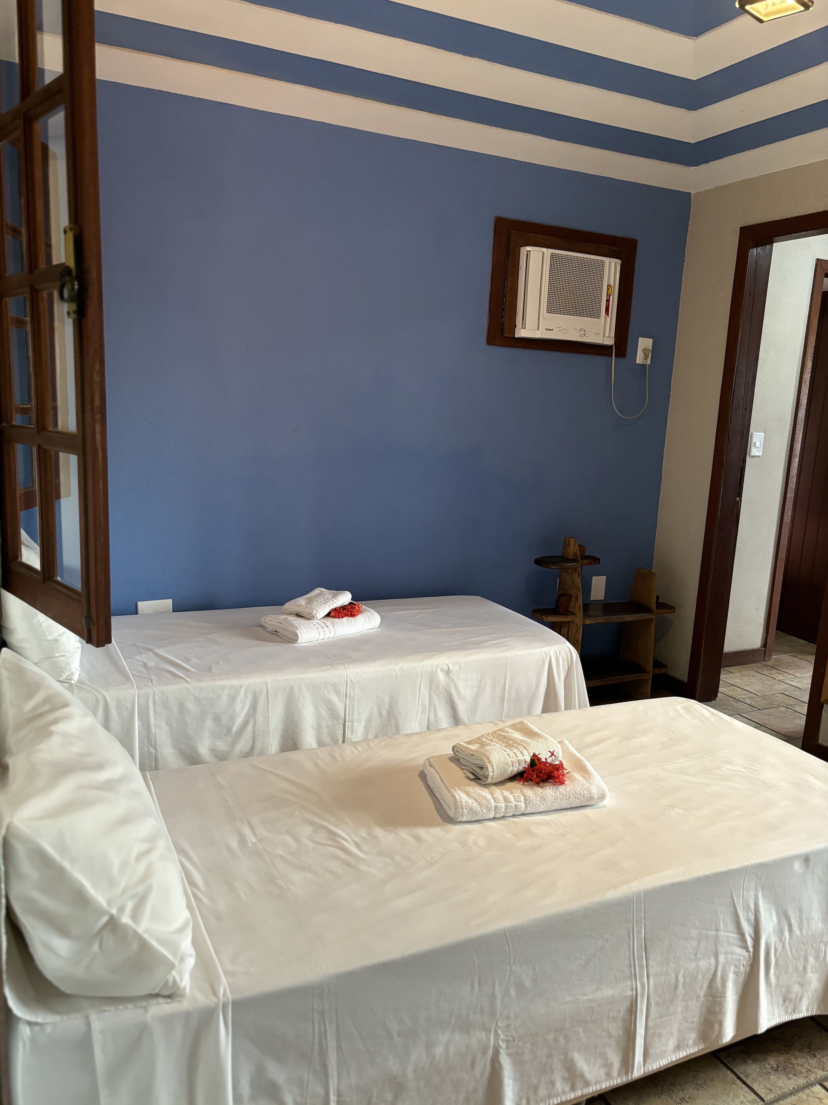 A hotel room with two beds, white linens, a blue wall, and an air conditioning unit.