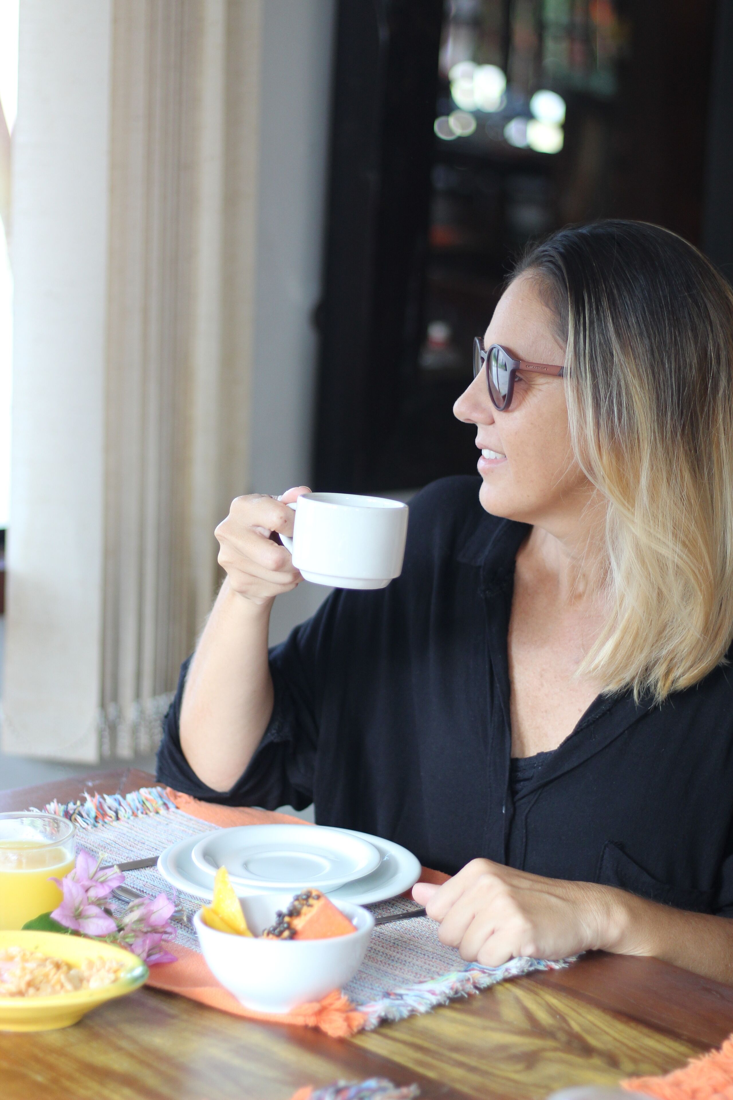 A person sitting at a table with a white cup, a bowl of food, and a plate.