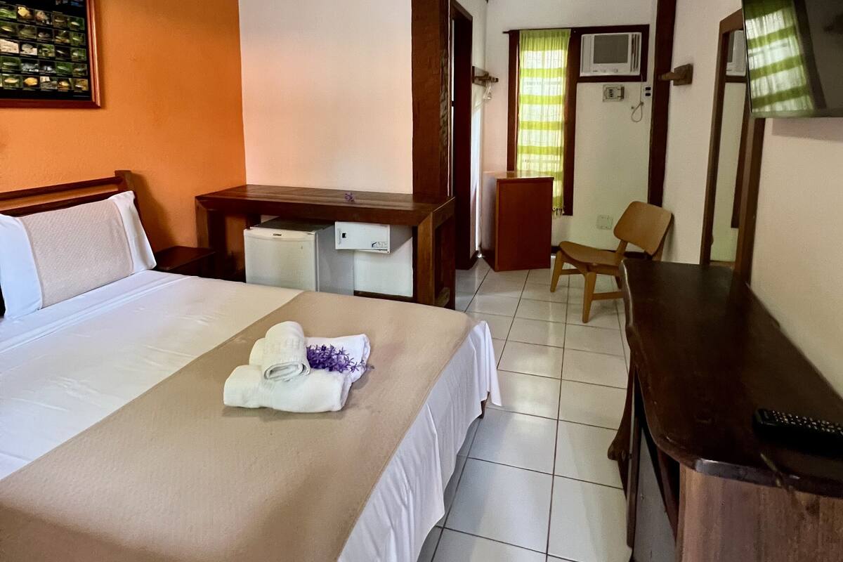 Une chambre d’hôtel avec un lit, un bureau, une chaise, une télévision et une fenêtre avec des rideaux.