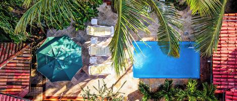 An aerial view of a rooftop pool area with a blue pool, lounge chairs, and a green umbrella.
