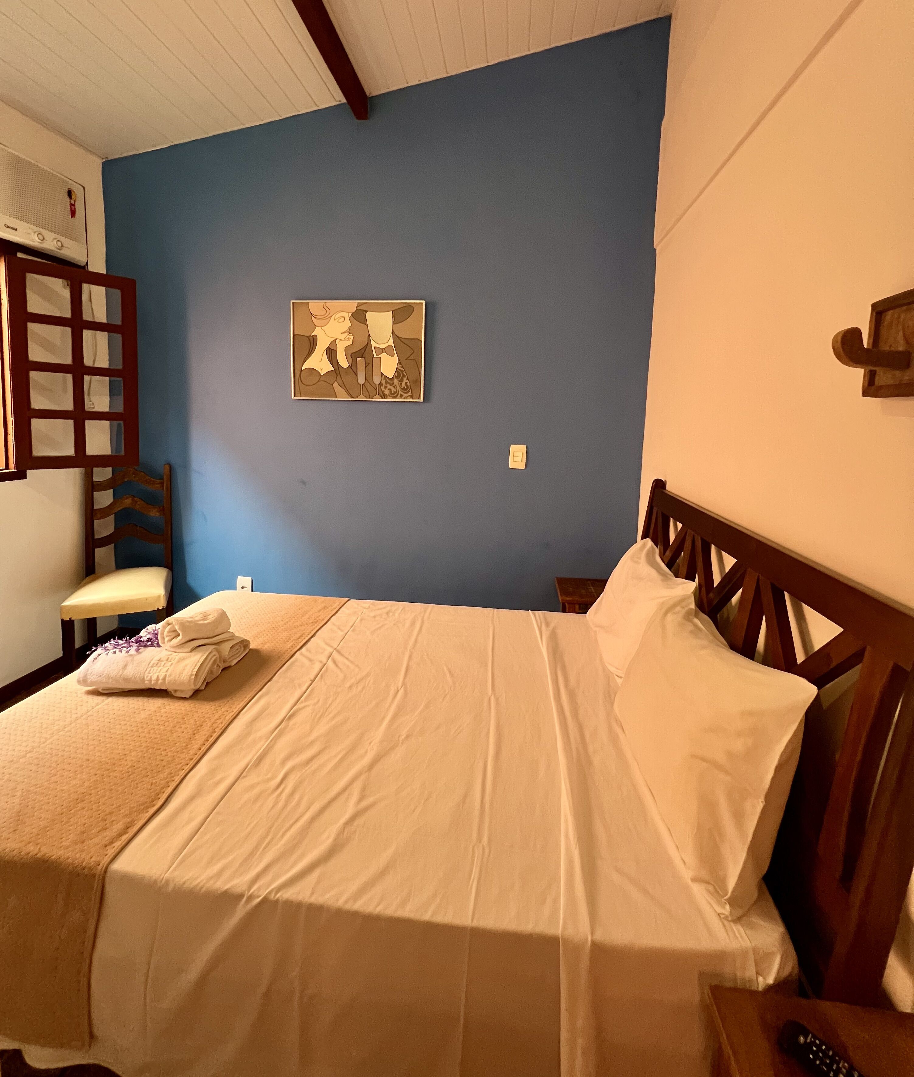 Un dormitorio con cama, una silla, un cuadro y un cabecero de madera.