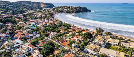 An aerial view of a coastal town with a beach, houses, and a hilly background.