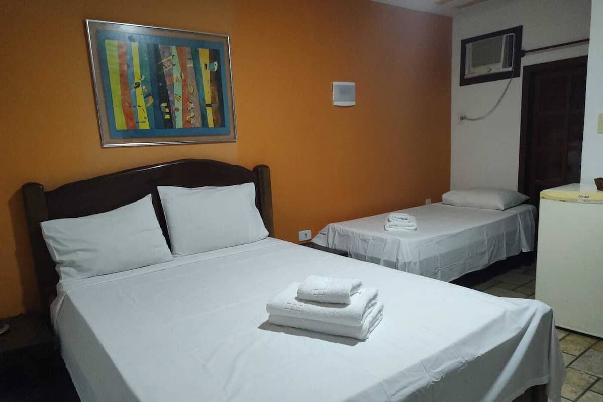 Une chambre d’hôtel avec un grand lit, deux petits lits, un bureau, une télévision et un tableau au mur.