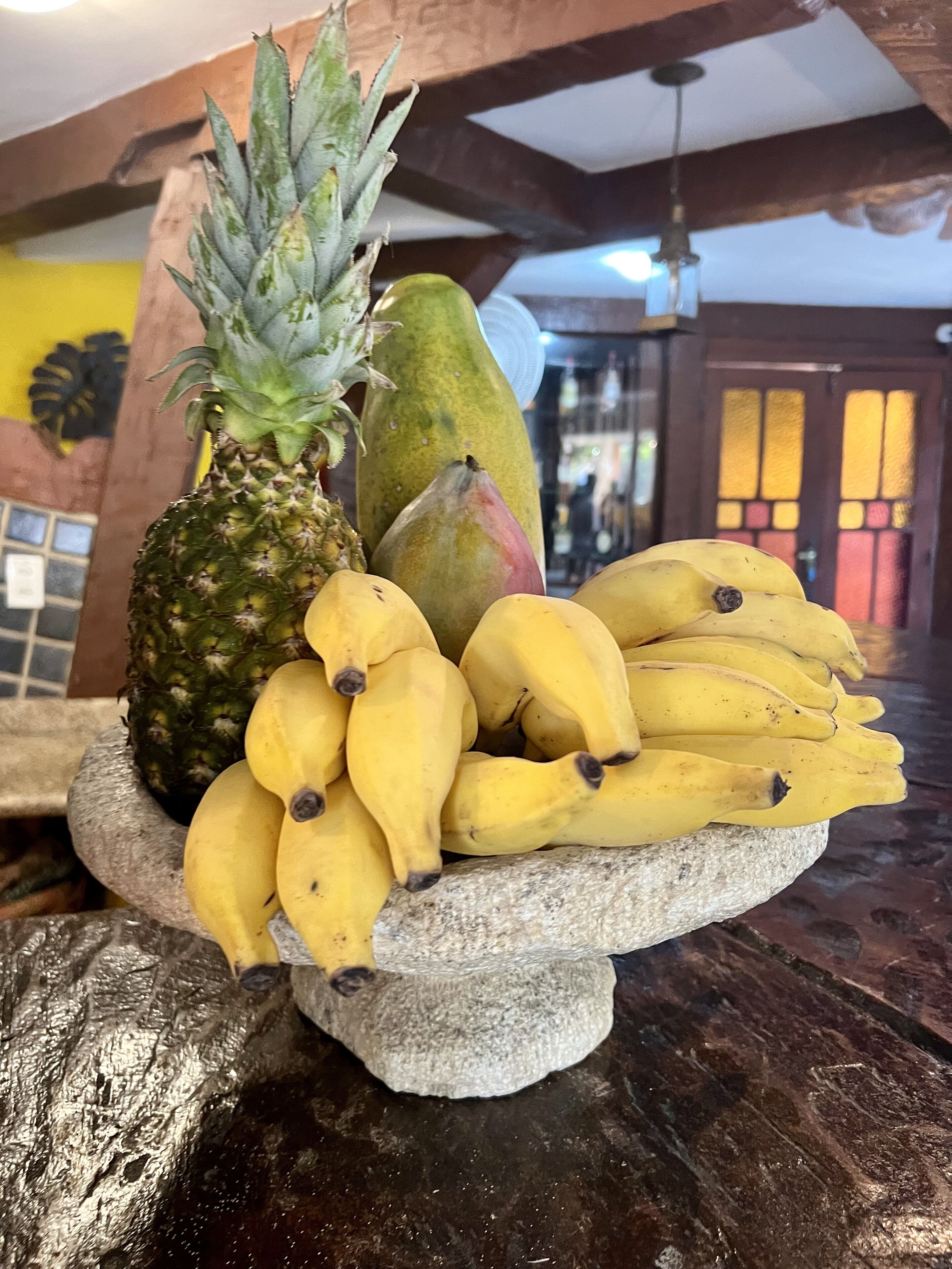 A stone fruit stand with a pineapple, mango, and bananas on a table.