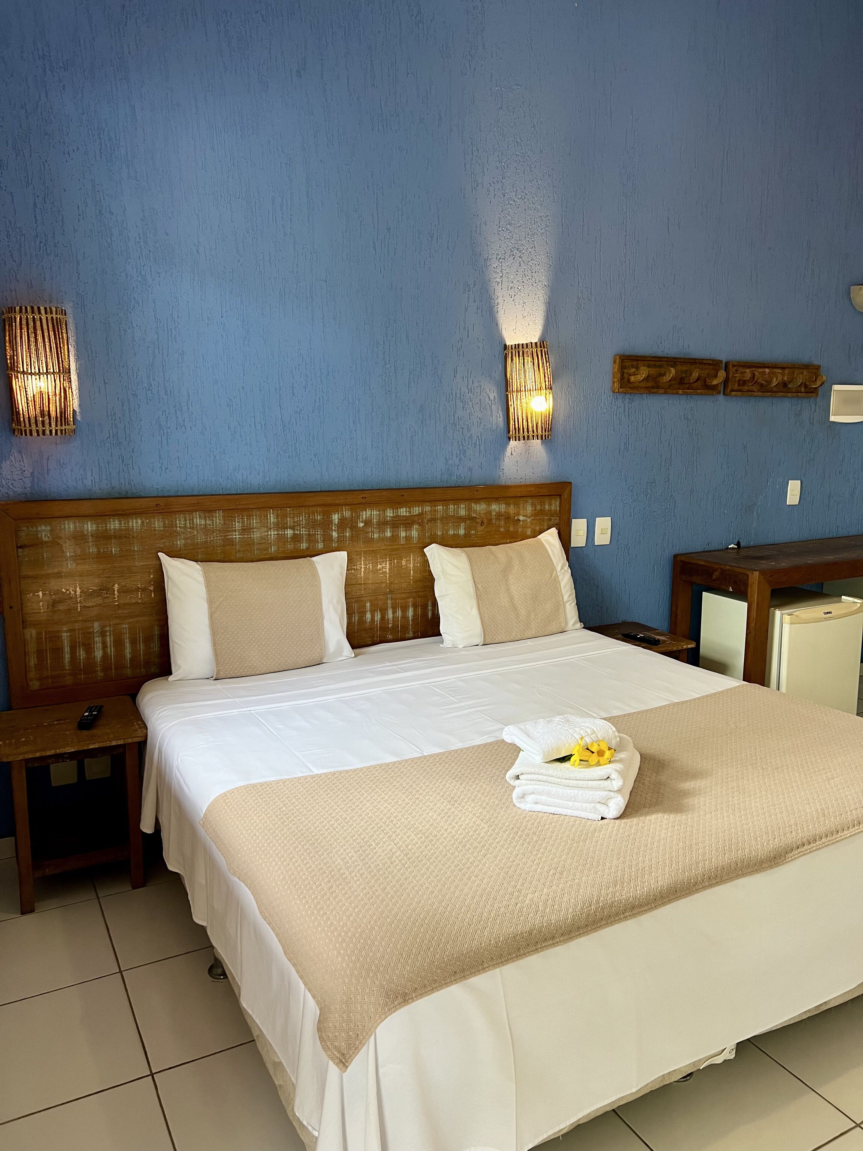 A hotel room with a large bed, two bedside tables, a nightstand, a small desk, and a refrigerator.