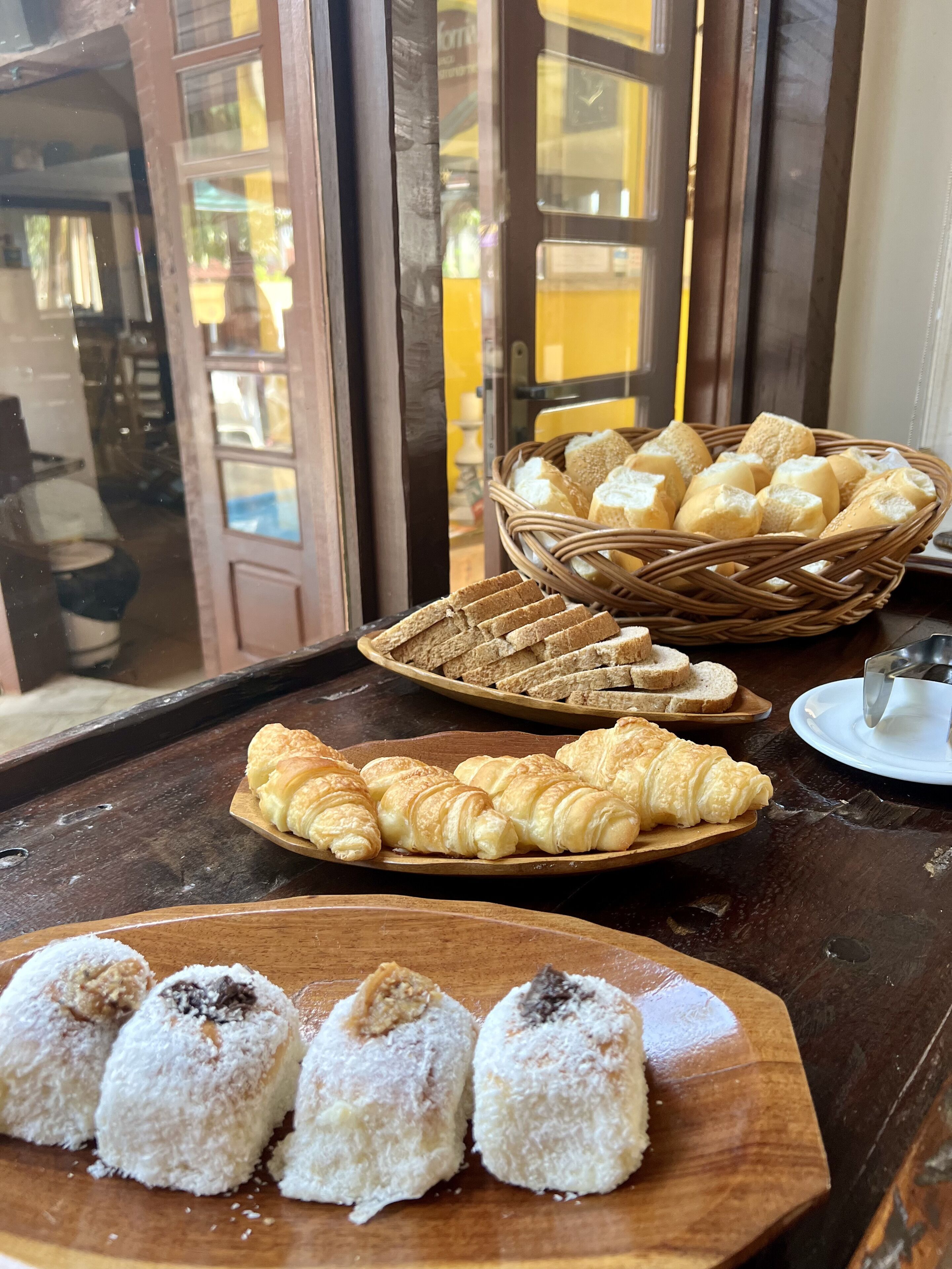 Una mesa con diversas opciones de panadería, incluyendo pan, cruasanes y pasteles cubiertos de coco.