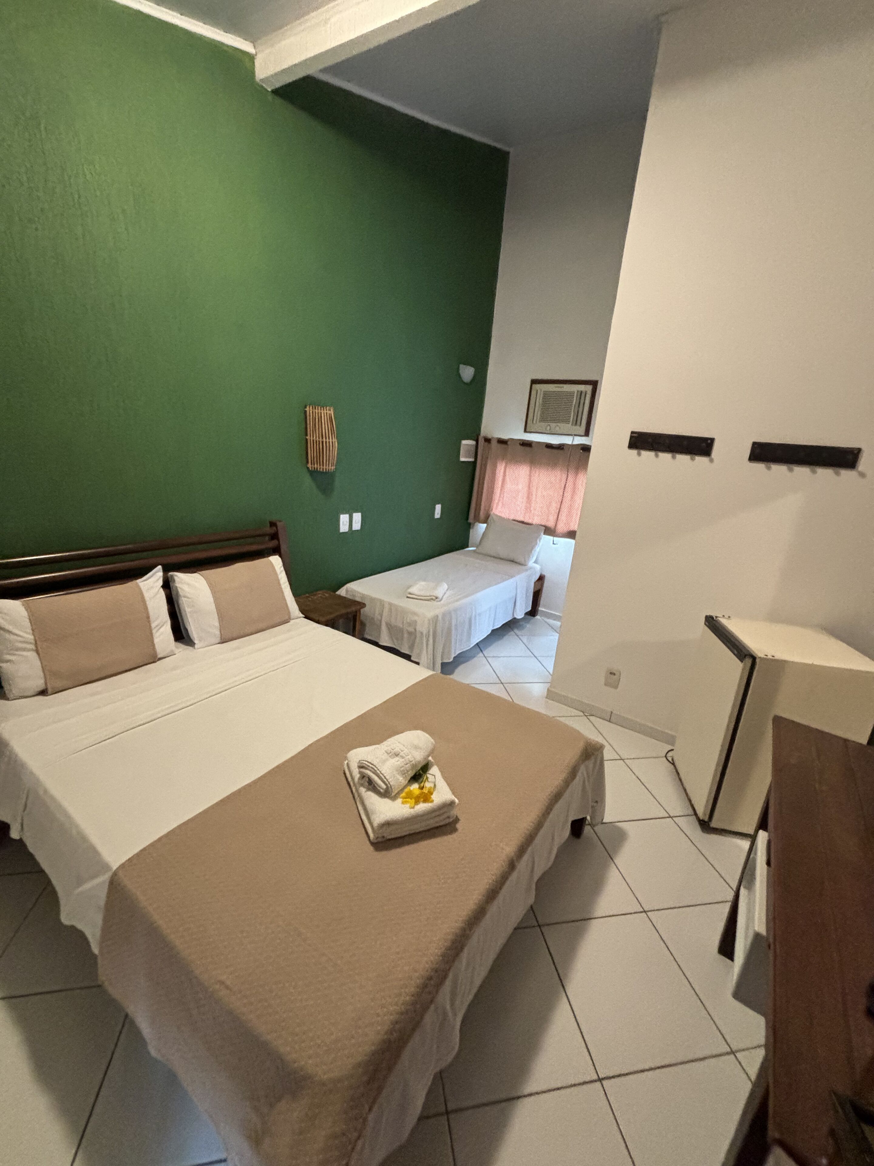 A hotel room with a large bed, a smaller bed, a desk, and a green wall.