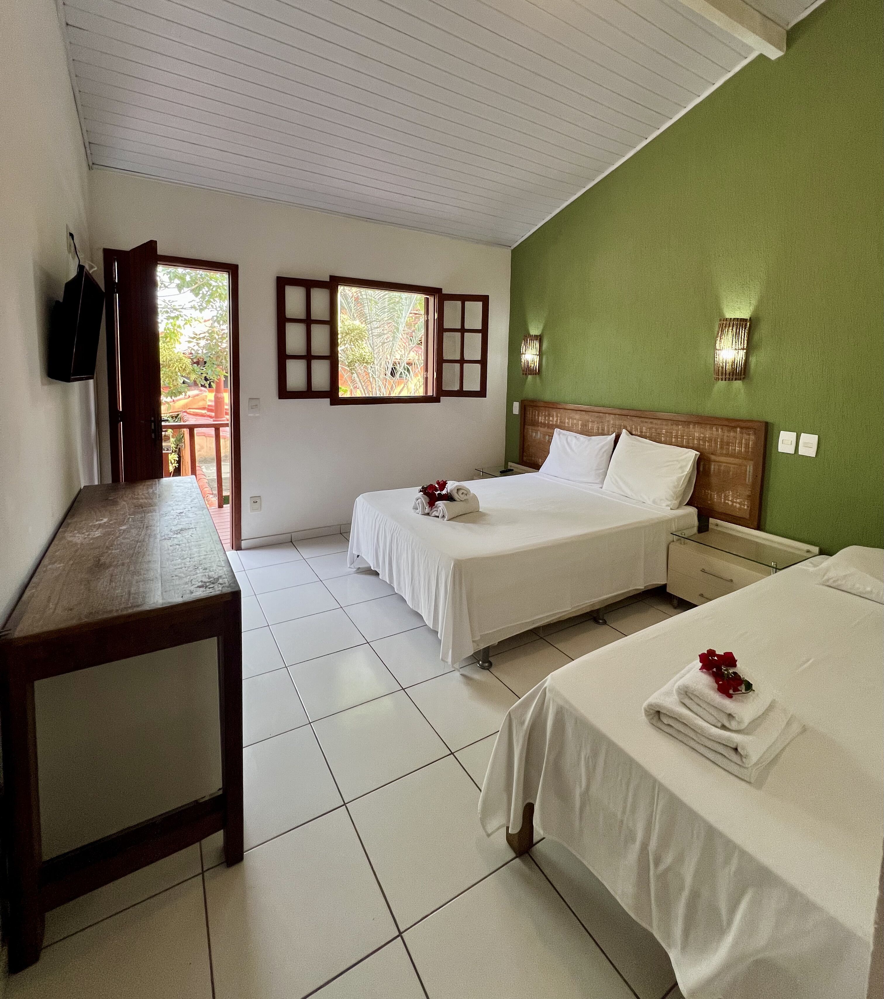 Habitación de hotel con dos camas, una mesa de madera, un televisor y una ventana con vistas a zonas verdes.