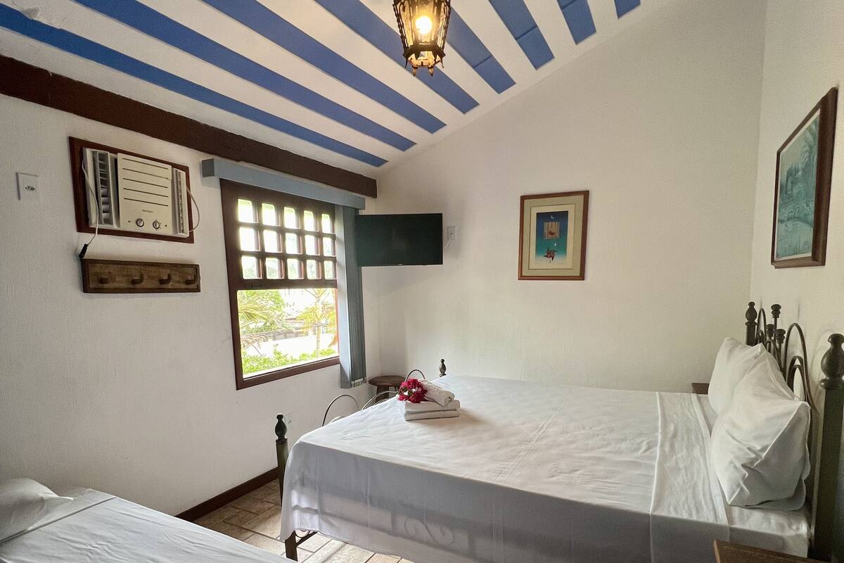 Une chambre d’hôtel avec deux lits, un ventilateur de plafond, un téléviseur fixé au mur et une fenêtre donnant sur un paysage verdoyant.