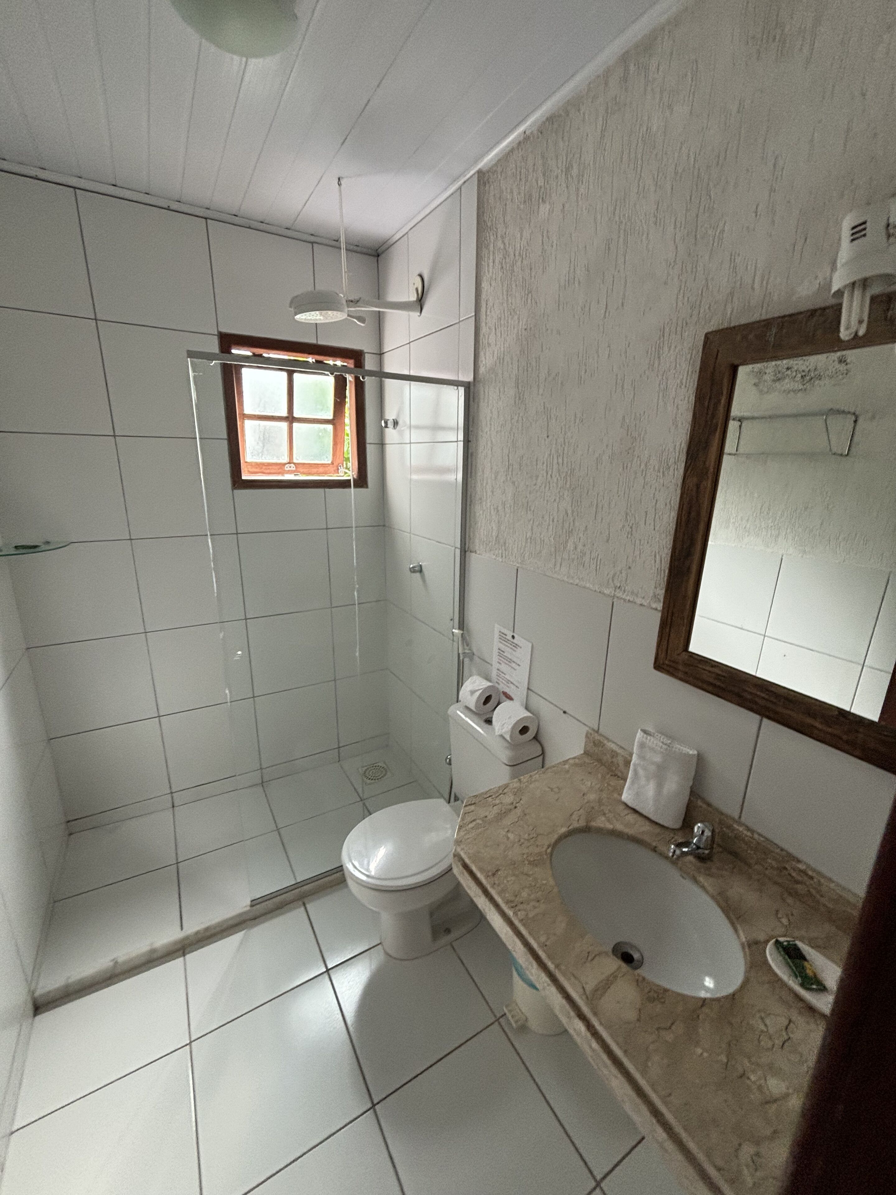 A bathroom with a toilet, sink, shower, and a small window.