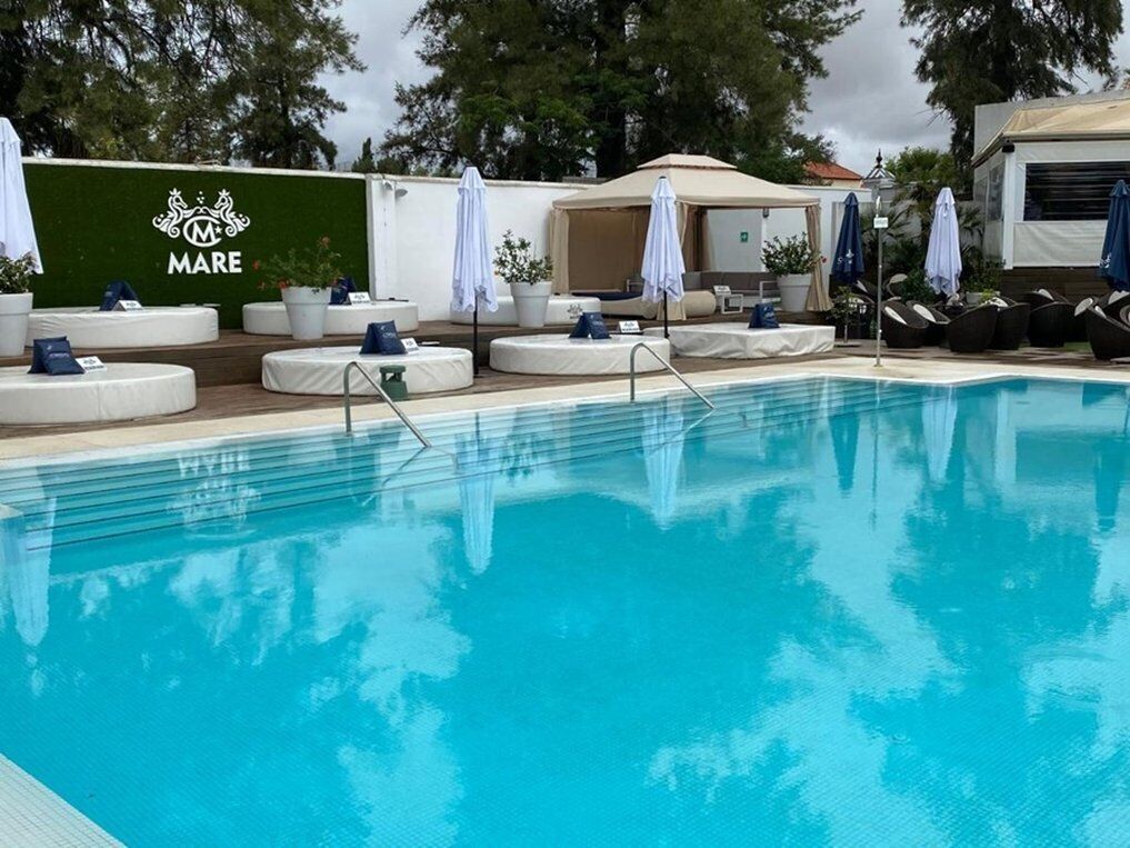 Una piscina con lettini e ombrelloni, un muro verde con il logo 'Mare' e una zona relax coperta.