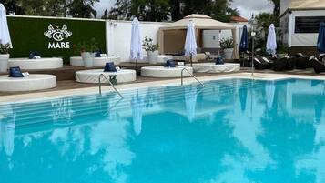 Una piscina con lettini e ombrelloni, un muro verde con il logo 'Mare' e una zona relax coperta.