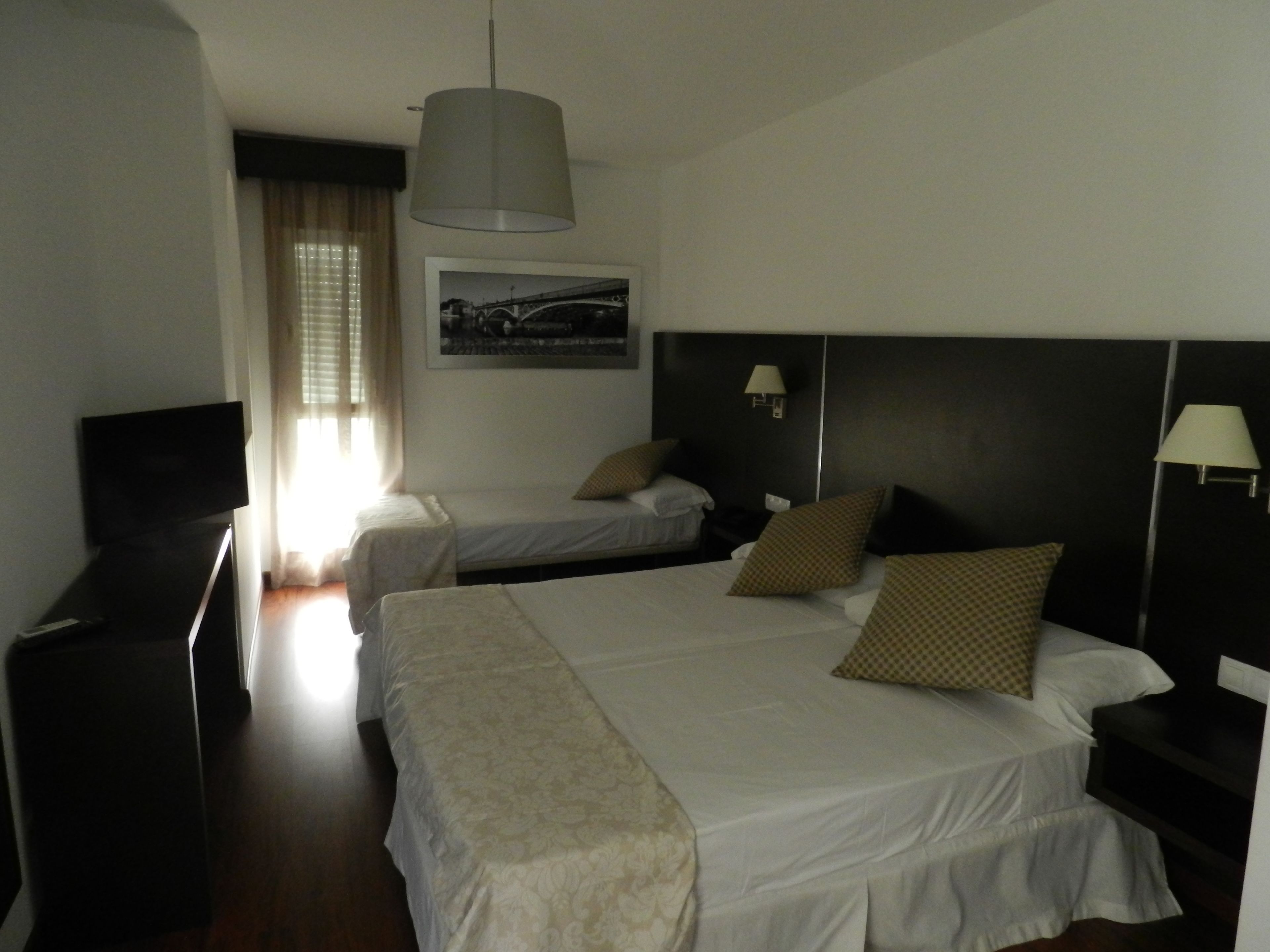 A hotel room with two beds, a television, a desk, and a window with curtains.