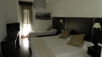 A hotel room with two beds, a television, a desk, and a window with curtains.