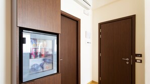 Una habitación con puerta de madera, un minibár con puerta de cristal y suelo de madera.