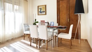 Un comedor con una mesa de madera, sillas blancas, una planta en maceta y un cuadro en la pared.
