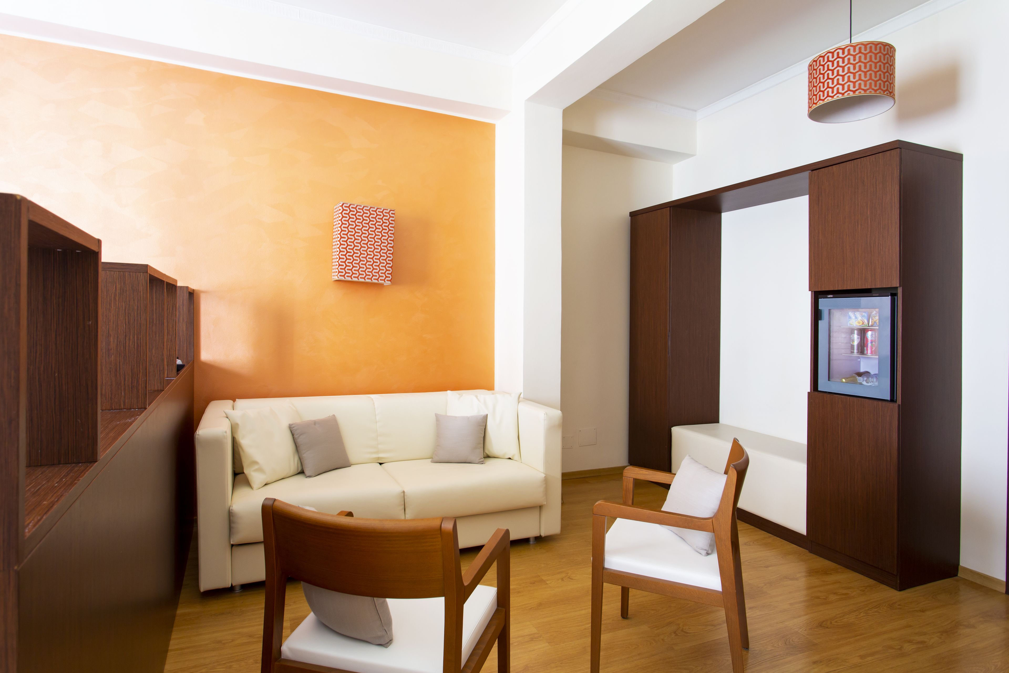 Ein modernes Wohnzimmer mit einer Couch, zwei Sesseln, einer Holzkommode und einem an der Wand befestigten Fernseher.