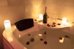 Una vasca da bagno con petali di rosa, candele e bicchieri da champagne.