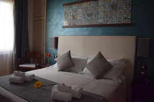 Een hotelkamer met een keurig opgemaakt bed, een stoel, een wand met een bloemendecor van tegels en een tafeltje met een bloevas.