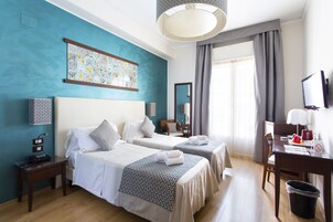 Habitación de hotel con dos camas, un escritorio, una silla, un televisor y un ventanal con cortinas.