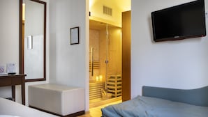 Habitación de hotel con cama, escritorio con silla, televisor montado en la pared y puerta de madera que da a un área de ducha.