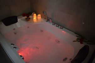 Una vasca da bagno illuminata da una luce rossa, due candele e un bouquet di fiori.
