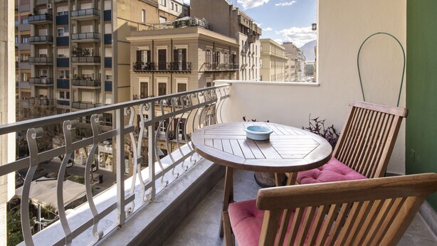 Un balcón con una mesa redonda y una silla, con vistas a un paisaje urbano con varios edificios.
