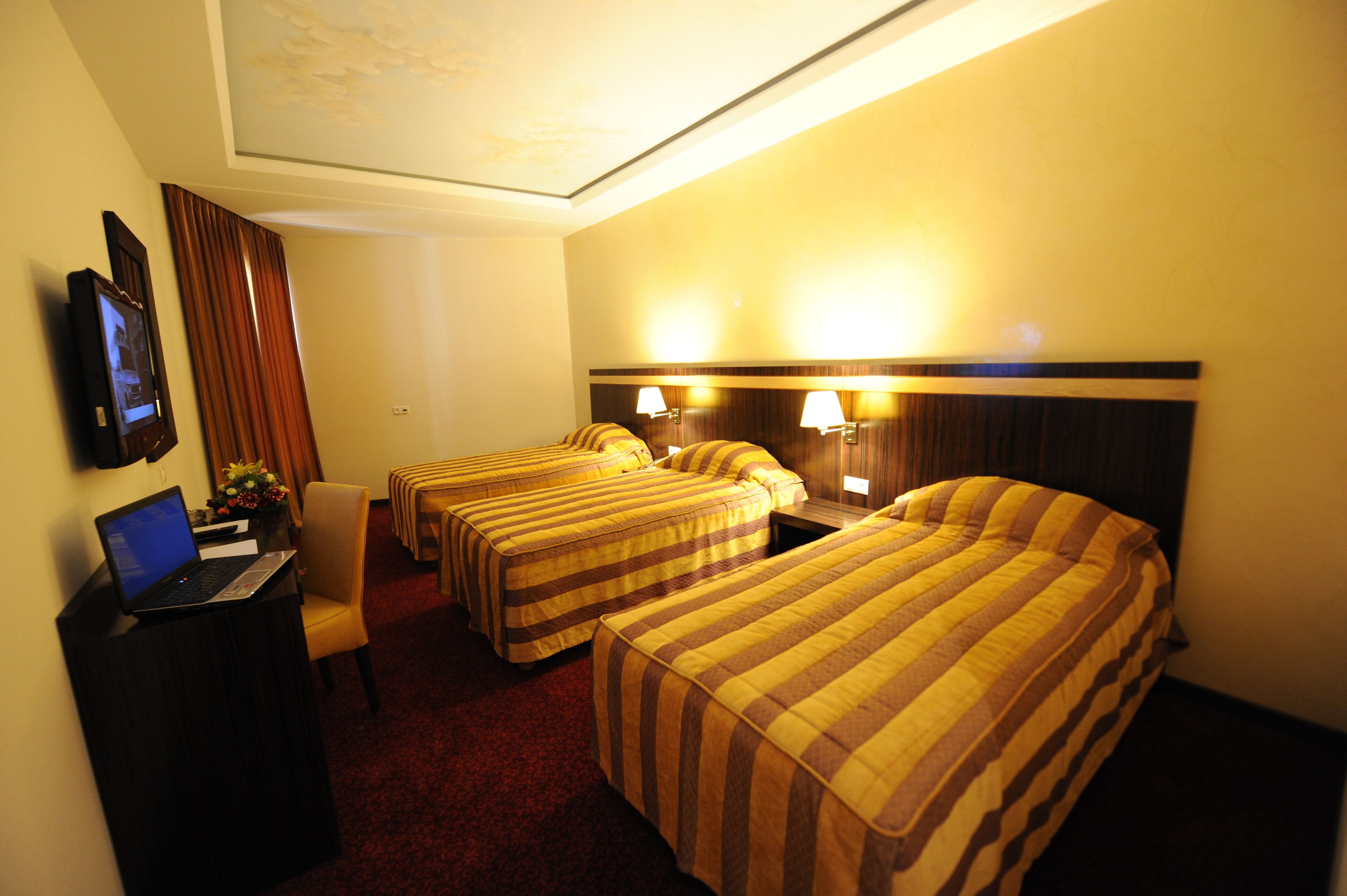 Ein Hotelzimmer mit zwei Einzelbetten, einem Schreibtisch mit Laptop, einem Fernseher und einer Schreibtischlampe.